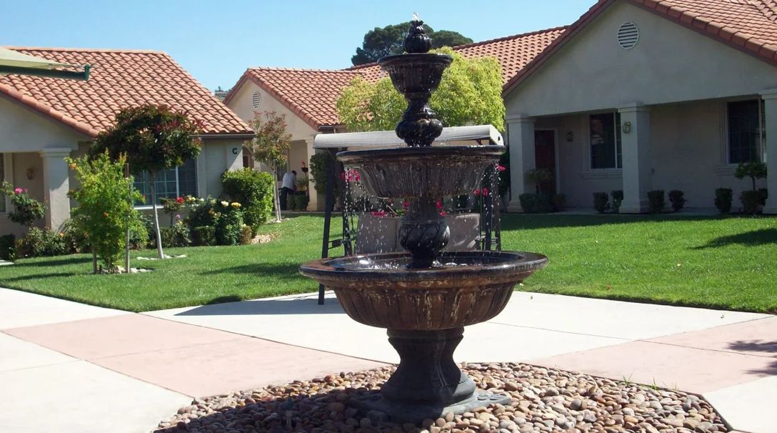 A two-tiered fountain in a garden setting with houses and a well-maintained lawn.