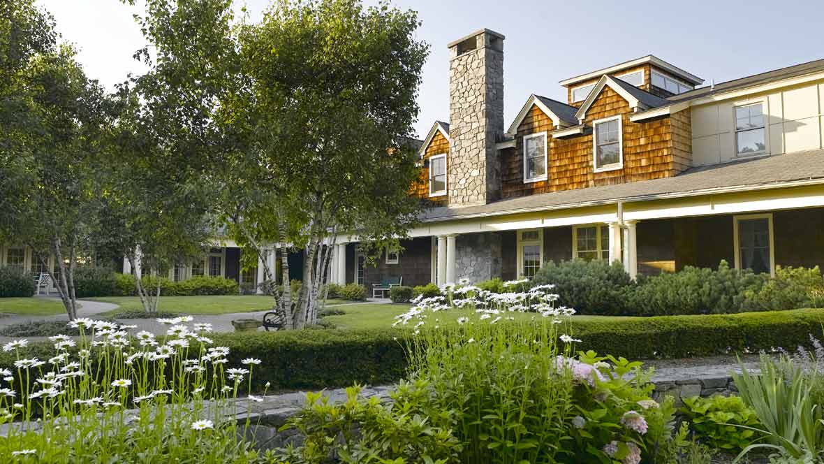 A beautiful house with a lush garden and a prominent chimney, surrounded by trees and flowers.