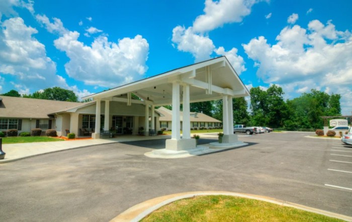 A building with a covered entrance and driveway, set against a partly cloudy sky.
