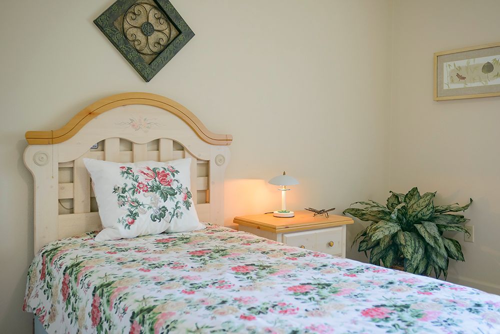 A cozy bedroom with a single bed featuring floral bedding, accompanied by a nightstand and a lamp.