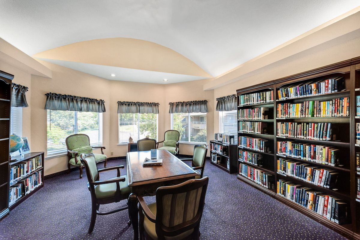 A cozy library room with bookshelves, a meeting table, and several chairs.