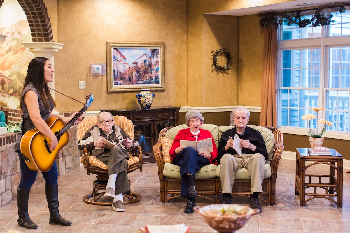 An elderly group enjoying a live guitar performance in a cozy living room setting.