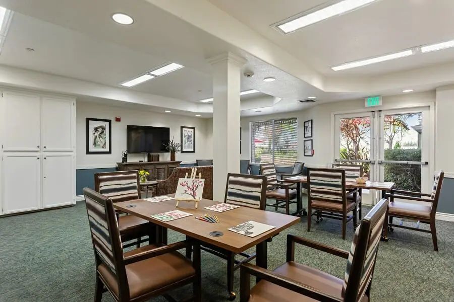 A modern dining area with wooden tables and chairs, featuring large windows and bright lighting.