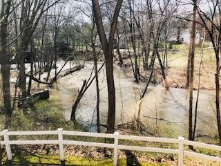 A flooded river surrounded by trees and a white fence.