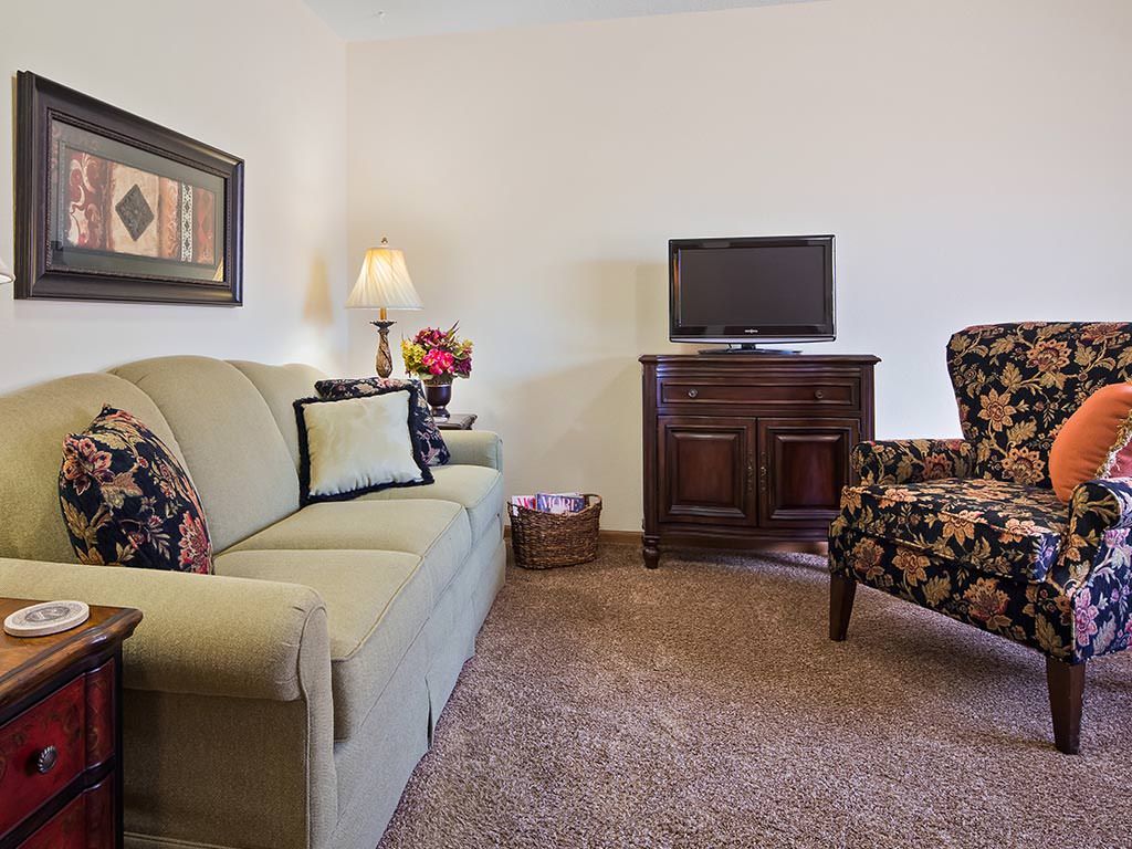A cozy living room with a sofa, armchair, television, and warm lighting.