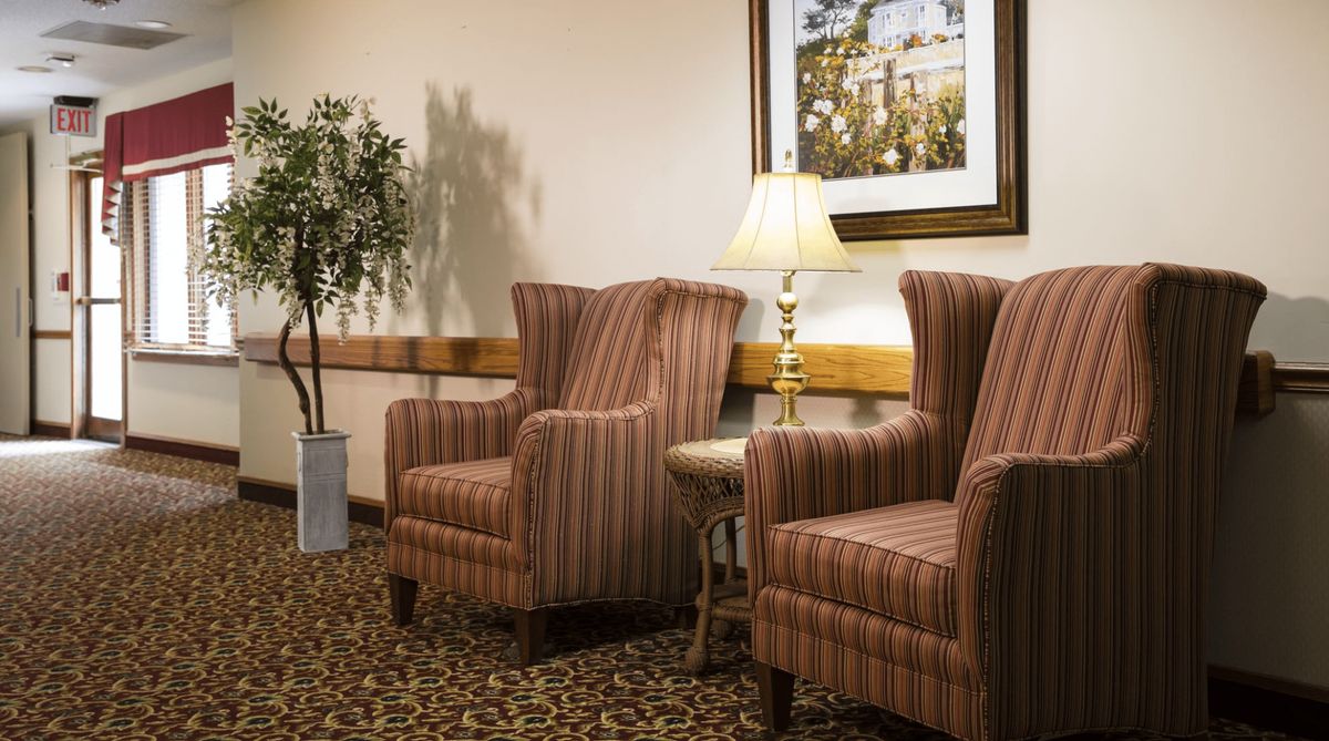 A cozy lobby area with two striped armchairs, a side table with a lamp, and decorative elements including a framed picture and a potted plant.