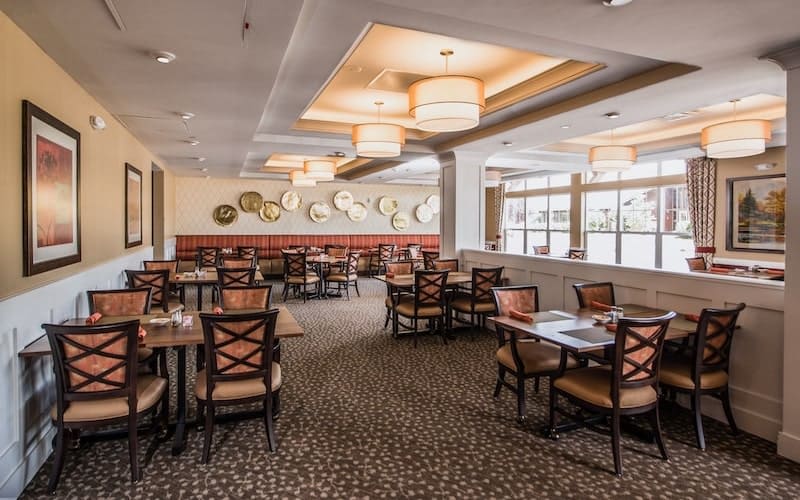 A spacious, elegantly designed restaurant dining area with neatly arranged tables and chairs, featuring stylish chandeliers and a patterned carpet.