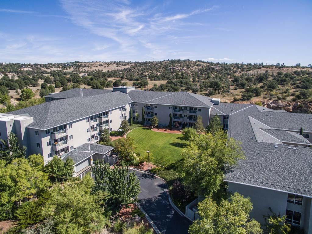 Aerial view of apartment buildings surrounded by lush greenery and a clear blue sky.