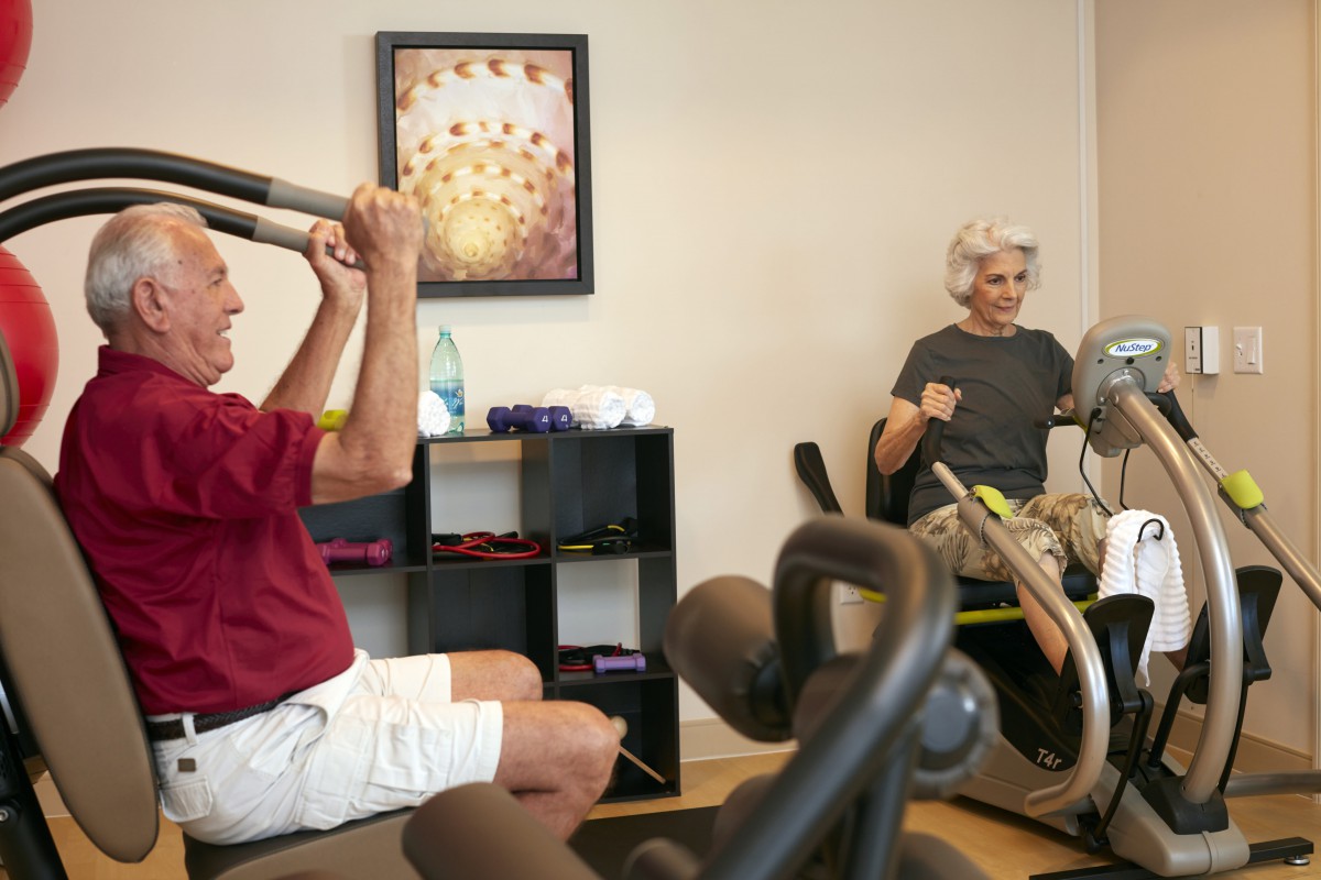 Two elderly individuals exercising in a gym setting.