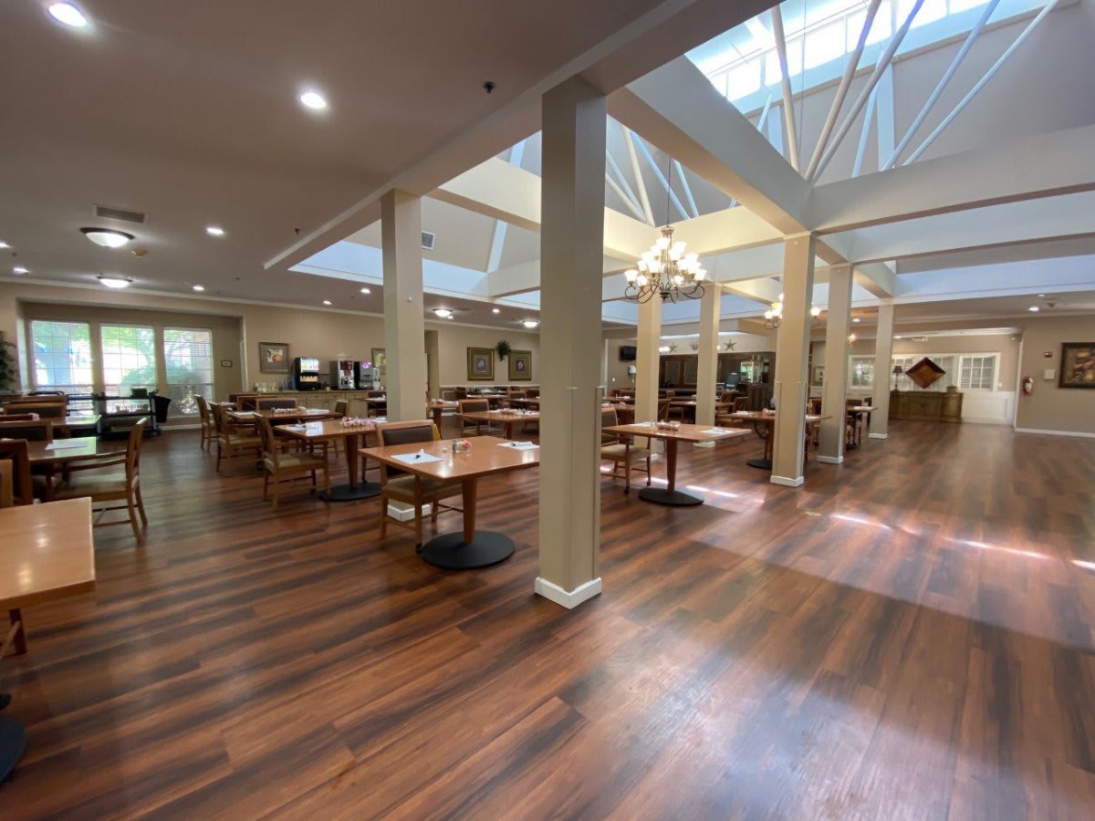 An empty dining area with wooden floors and skylights, featuring tables and chairs arranged neatly.