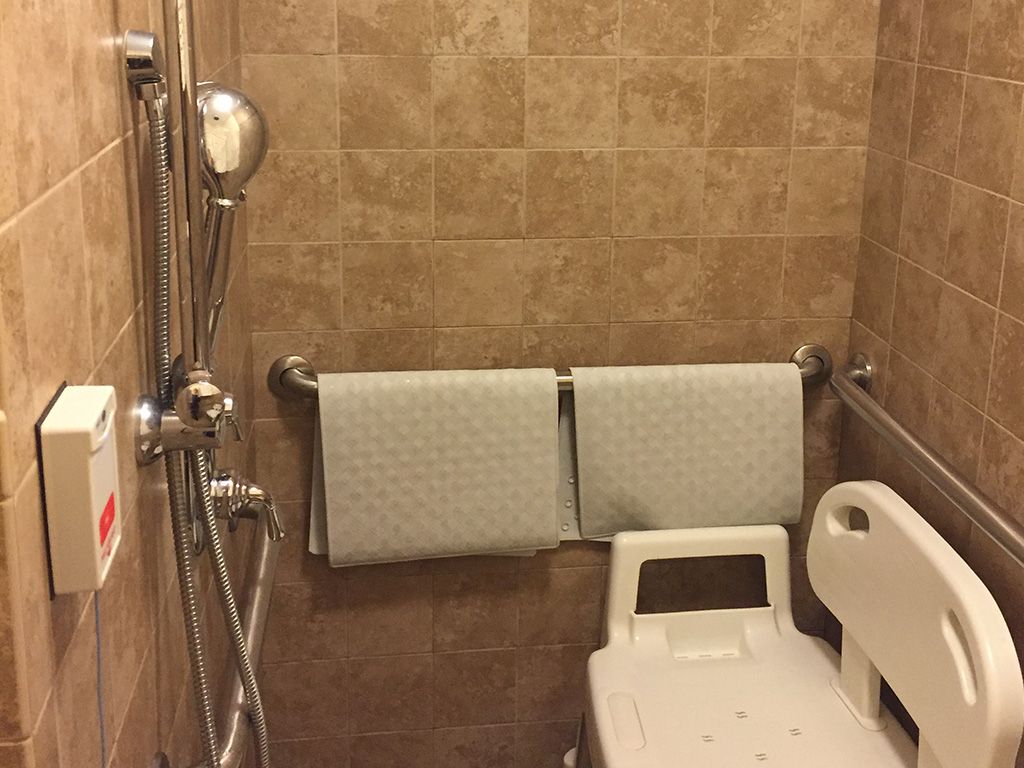 A shower area with tile walls, equipped with a shower chair, handrails, and two towels hanging on the wall.