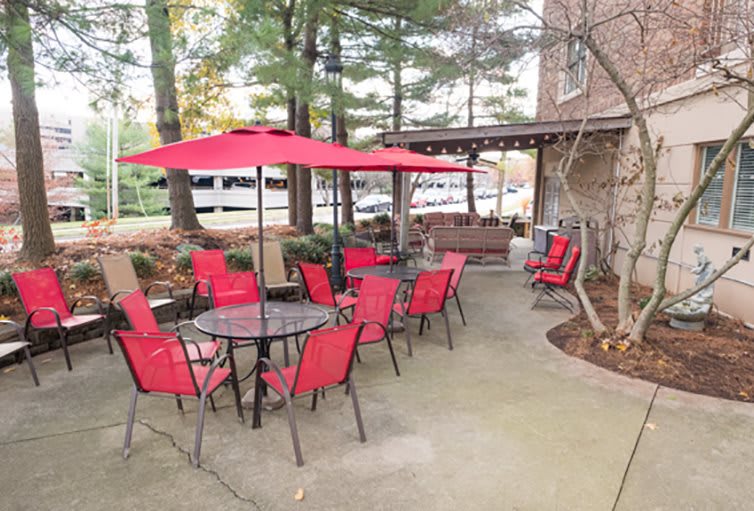 A cozy patio with red chairs and umbrellas, surrounded by trees and adjacent to a building.