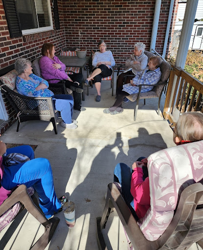 A group of seniors enjoying a sunny day together on the porch, engaged in conversation.