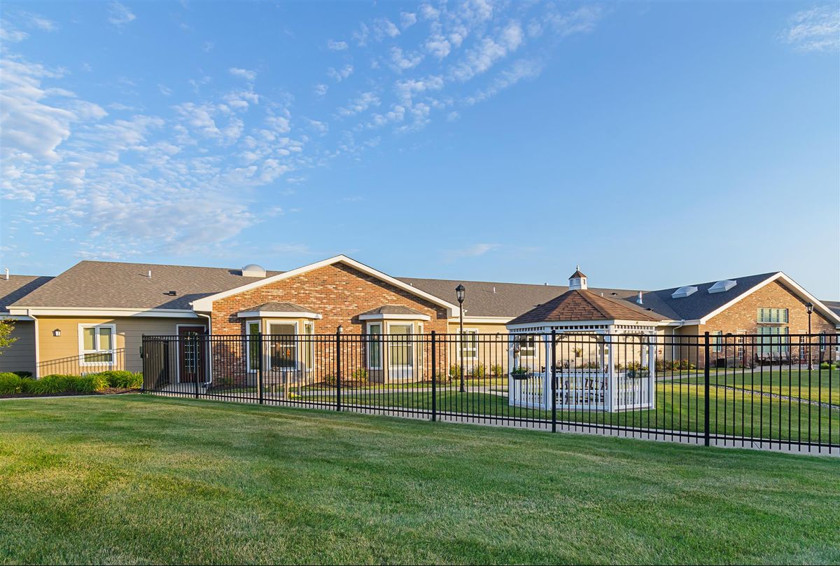 A spacious yard with a fence, gazebo, and a single-story house under a blue sky.
