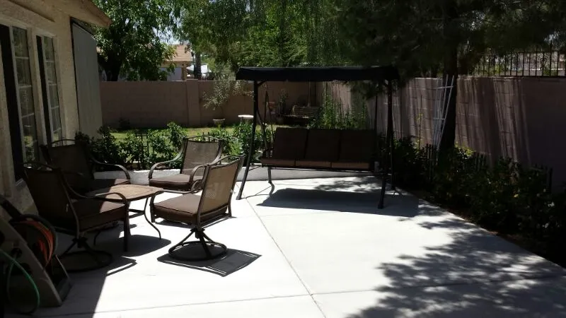 A sunny backyard patio with a swing chair, chairs, and a table.