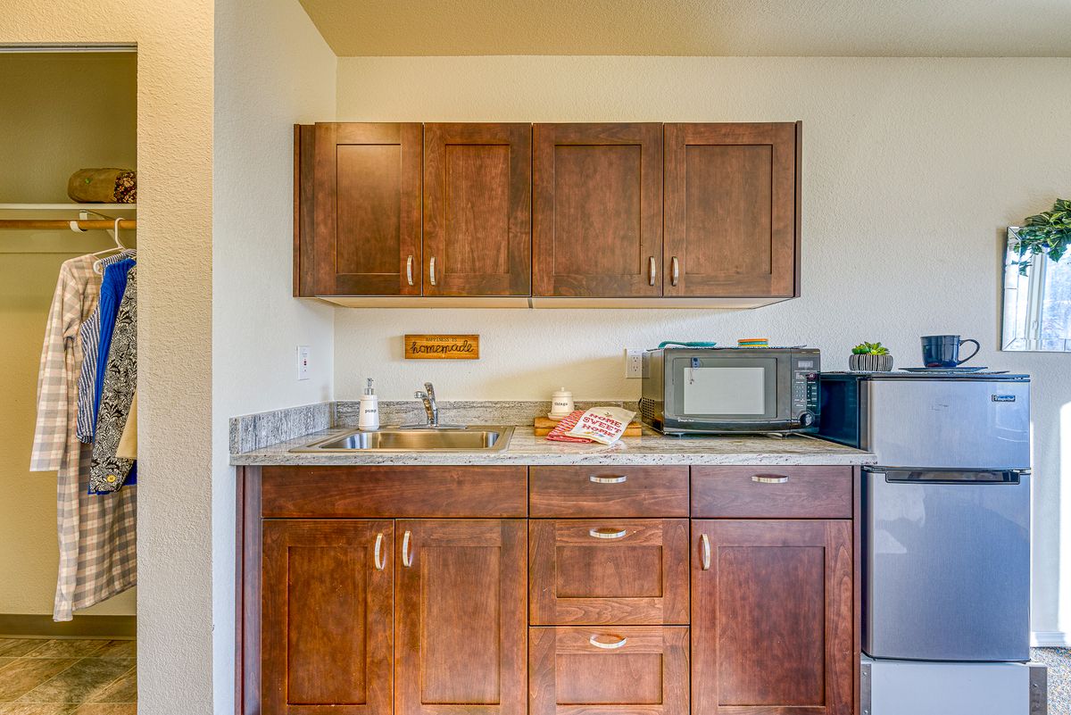 A compact kitchen area featuring wooden cabinets, a countertop with a sink, and a microwave.