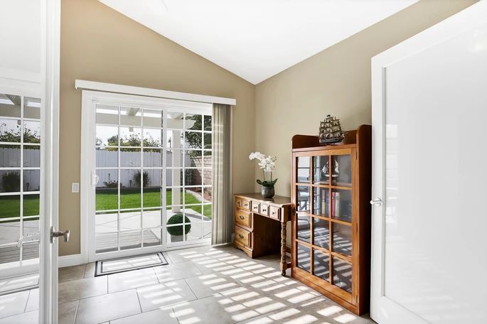 A bright and cozy living room with sliding glass doors, featuring a wooden cabinet and desk, enhanced by natural lighting.