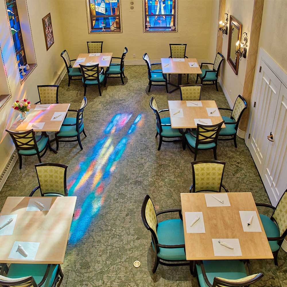 A cozy dining area with neatly arranged tables and chairs, featuring colorful light reflections from the windows.