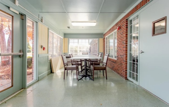 A cozy indoor dining area with a table and chairs, surrounded by windows and a brick wall.