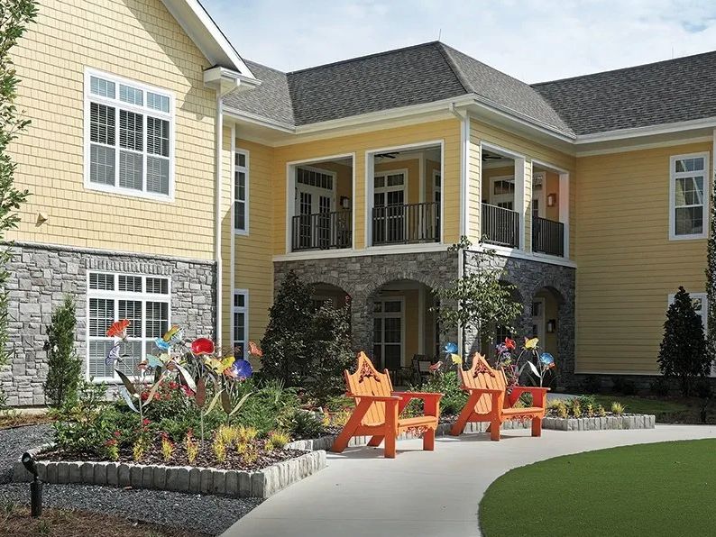 A yellow two-story building with stone accents, surrounded by a landscaped garden and colorful benches.