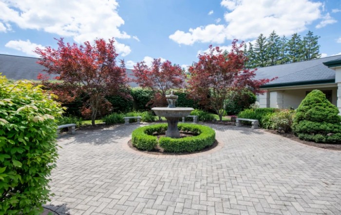 A beautifully landscaped garden featuring a central fountain surrounded by trees and a brick pathway.