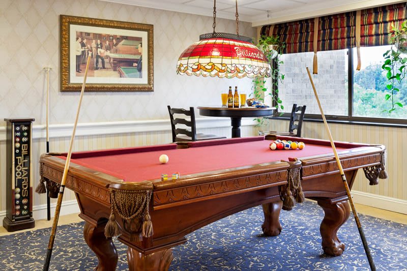 A cozy game room featuring a red felt pool table with two cues and an ornate hanging light.