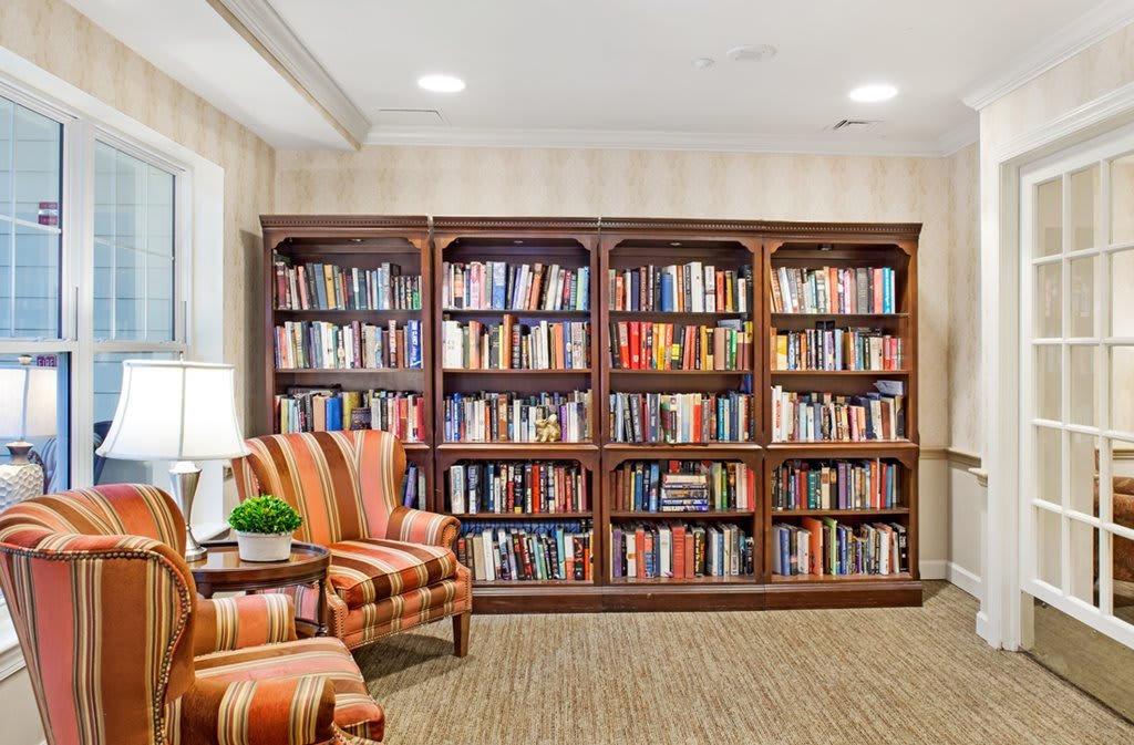 A cozy reading area with bookshelves filled with books, accompanied by a comfortable armchair and a lamp.