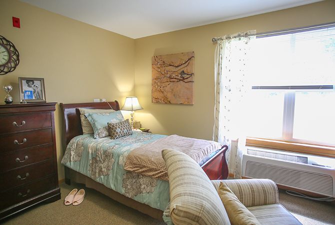 A cozy bedroom with a neatly made bed, soft lighting from a bedside lamp, and natural light streaming through the window.