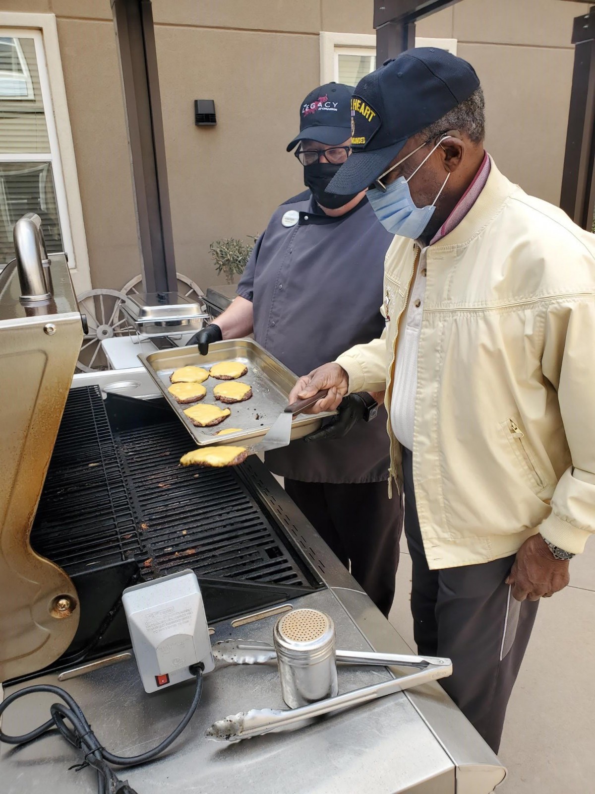 Two people grilling burgers on an outdoor barbecue.