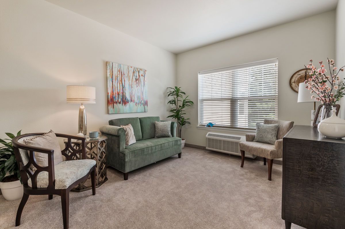 A cozy living room with a green sofa, armchairs, and a large window allowing natural light.