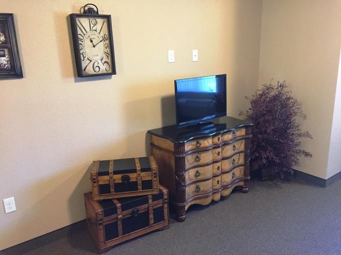 A cozy living room corner featuring a dresser with a television, decorative clock on the wall, and a stack of vintage-style trunks.
