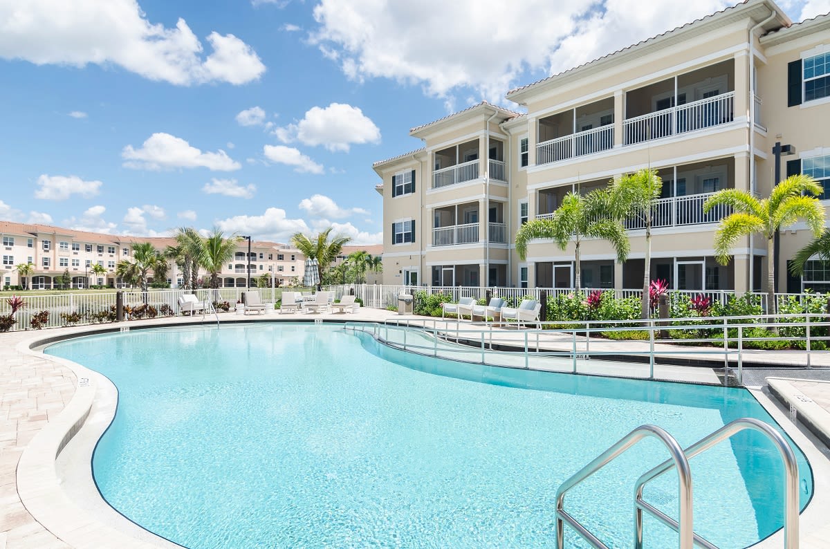 A modern residential complex with a large swimming pool surrounded by palm trees.