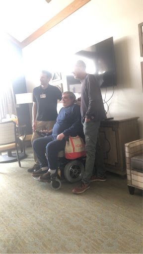 A group of friends posing together indoors, with one person in a wheelchair.