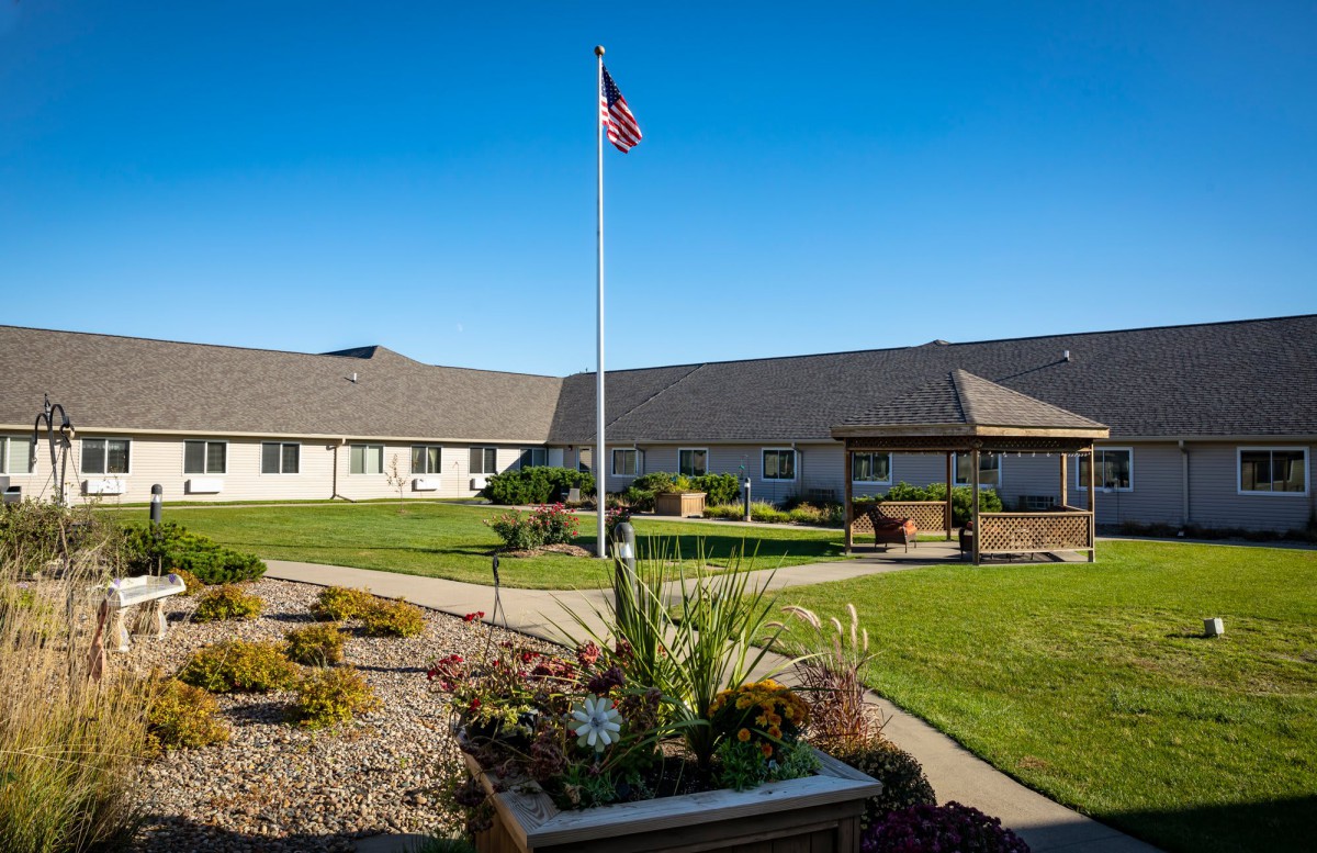 A well-maintained building with a flagpole and landscaped gardens under a clear blue sky.
