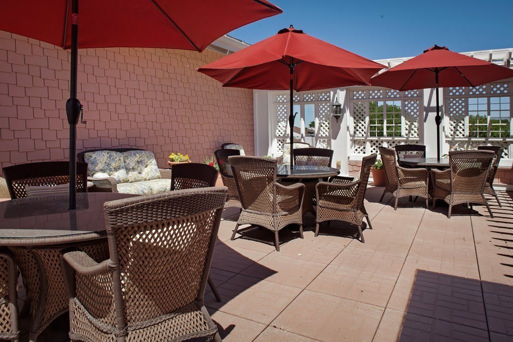 A cozy patio area with wicker chairs and red umbrellas on a sunny day.