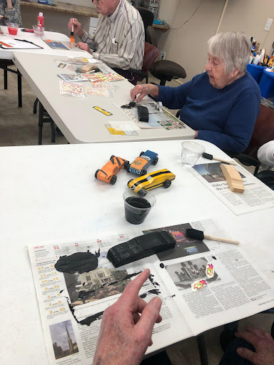 Seniors engaging in a creative painting session, working on toy vehicles at a communal table.