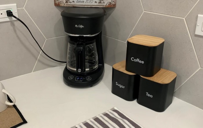 A kitchen countertop with a coffee maker and labeled canisters for coffee, sugar, and tea.