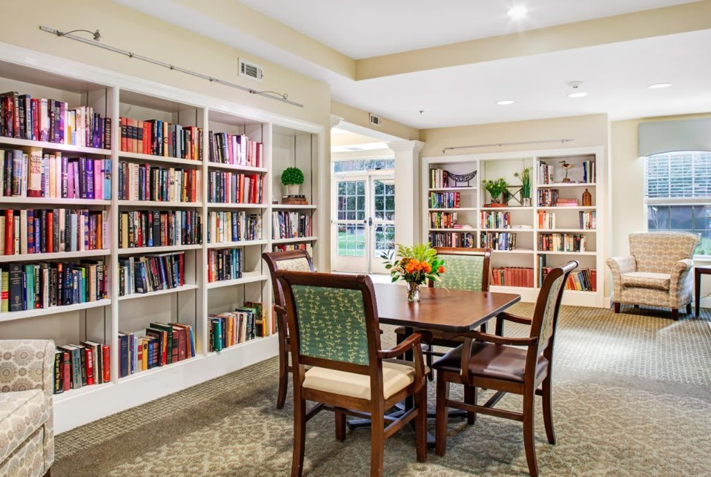 A cozy library setting with bookshelves, a central table, and chairs.