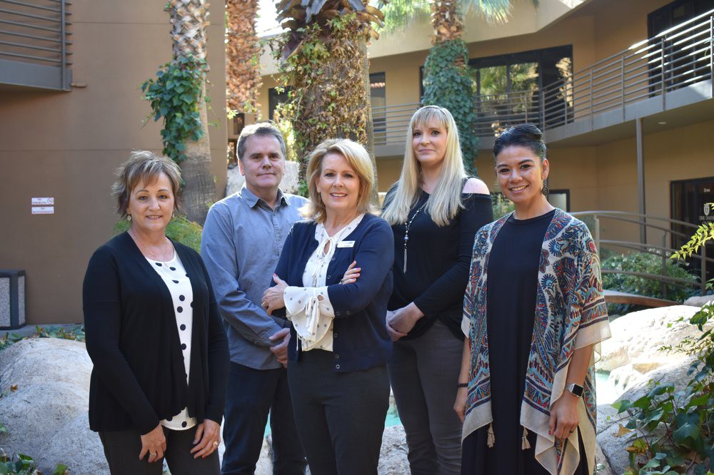 A group of five professionals standing outdoors in business attire.