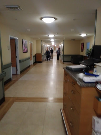 A view of a hospital corridor, featuring a reception area and patients walking in the distance.