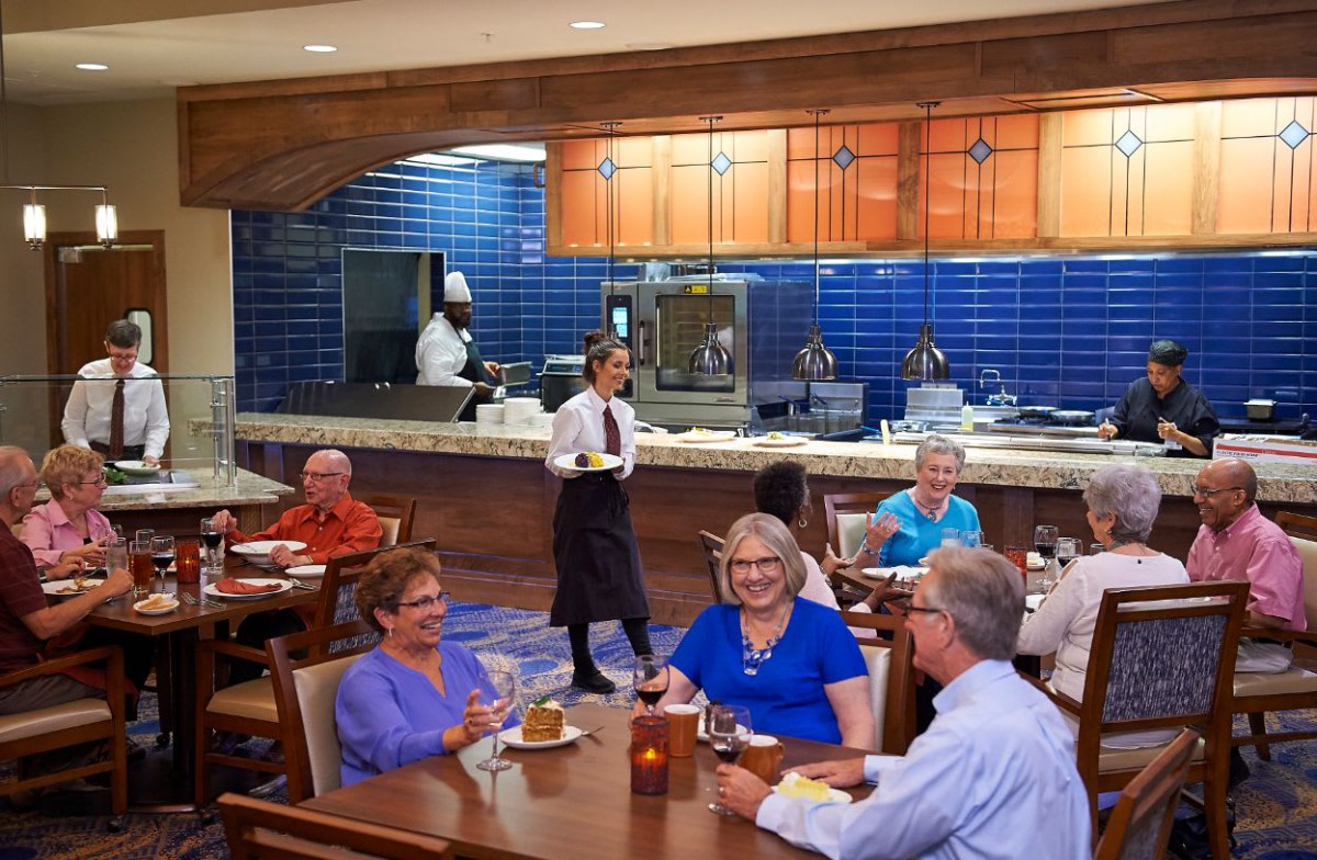 A group of people enjoying a meal at a restaurant with visible kitchen staff in the background.