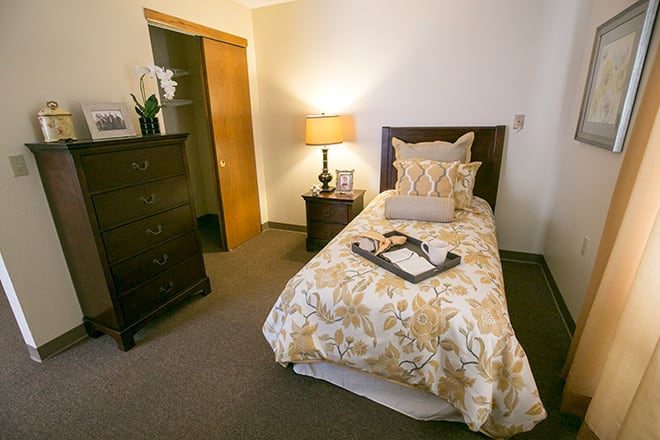 A cozy bedroom with a single bed adorned with decorative pillows next to a side table and lamp.