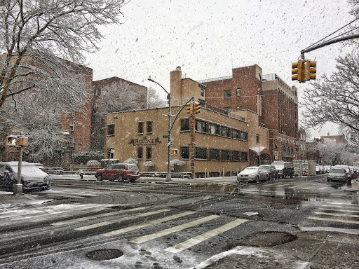 A snowy urban scene depicting a city street with traffic lights and buildings in the background.