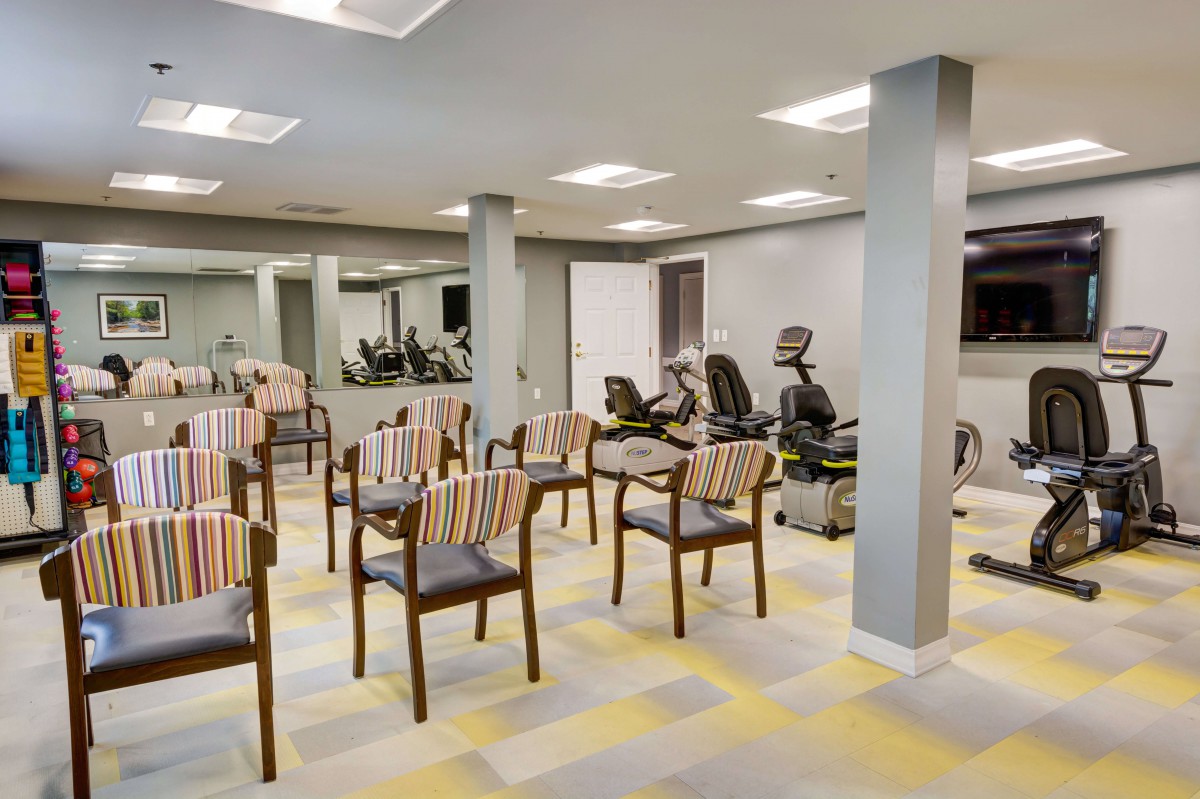 A modern exercise room featuring chairs arranged in rows and fitness equipment along the walls.