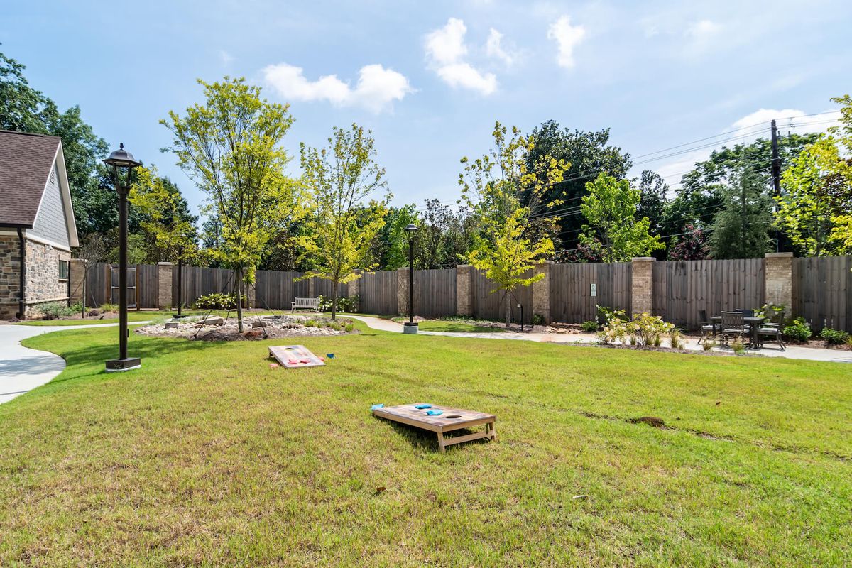 A backyard with cornhole boards set up on the grass, surrounded by trees and a wooden fence.