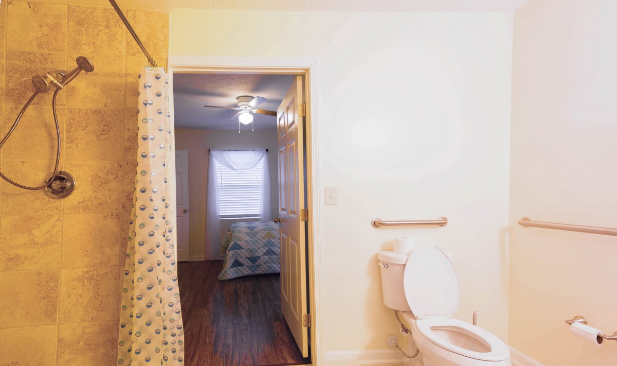 A view from the bathroom into a bedroom, featuring a toilet and a shower curtain.