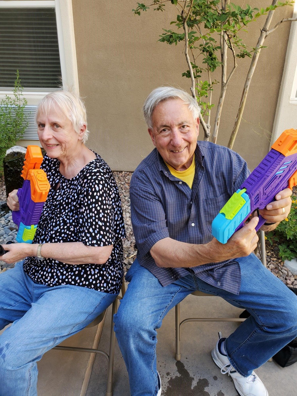 An elderly couple having fun with colorful water guns outdoors.