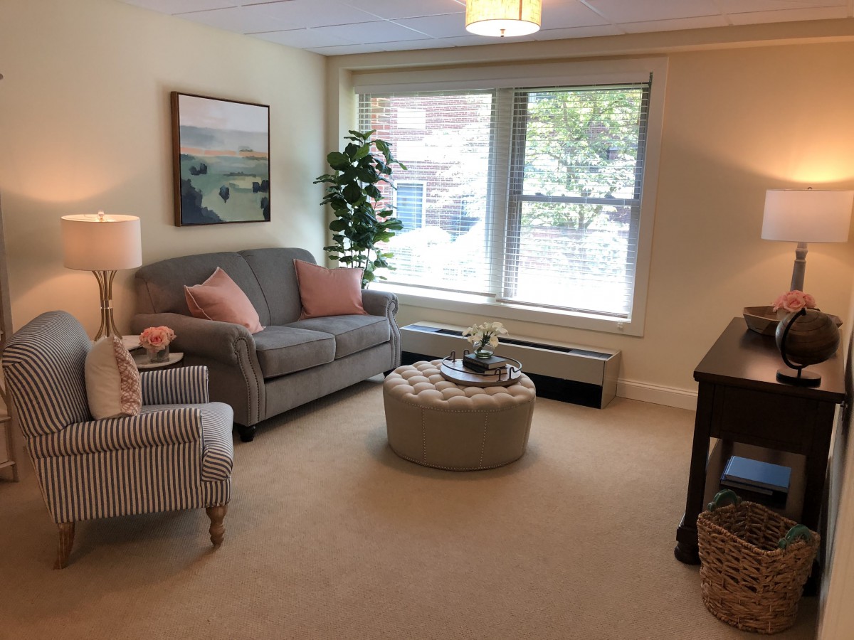 A cozy living room with a sofa, armchair, and round coffee table by a large window.