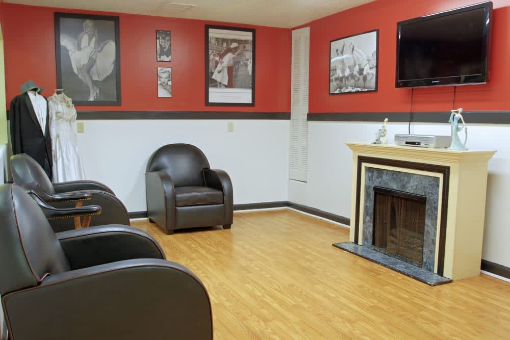 A modern waiting room with armchairs, a television, and a fireplace, featuring red and white walls.