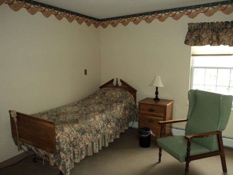 A small, cozy bedroom with a single bed, nightstand, and upholstered chair.